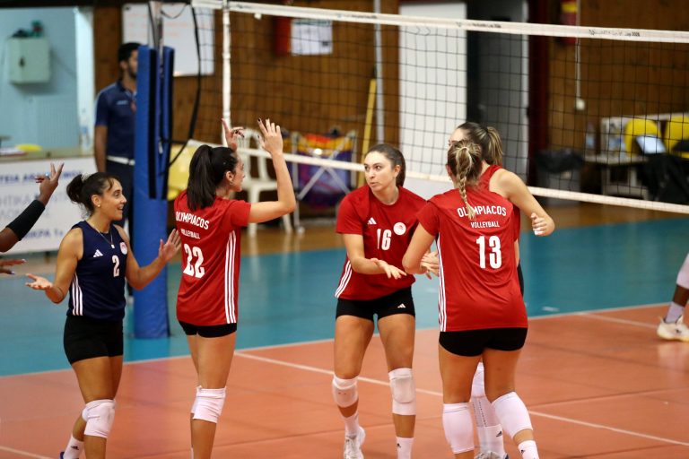 001 The Volley Lovers Group of female volleyball players in red jerseys celebrate on an indoor court near the net.