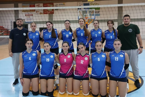 Girls' volleyball team posing for a group photo on the court, wearing blue uniforms with numbers, two players in pink jerseys kneeling in front.