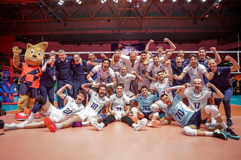 233601I8A4503 The Volley Lovers A large volleyball team and mascot celebrate together on the court, fists raised in triumph after a match.