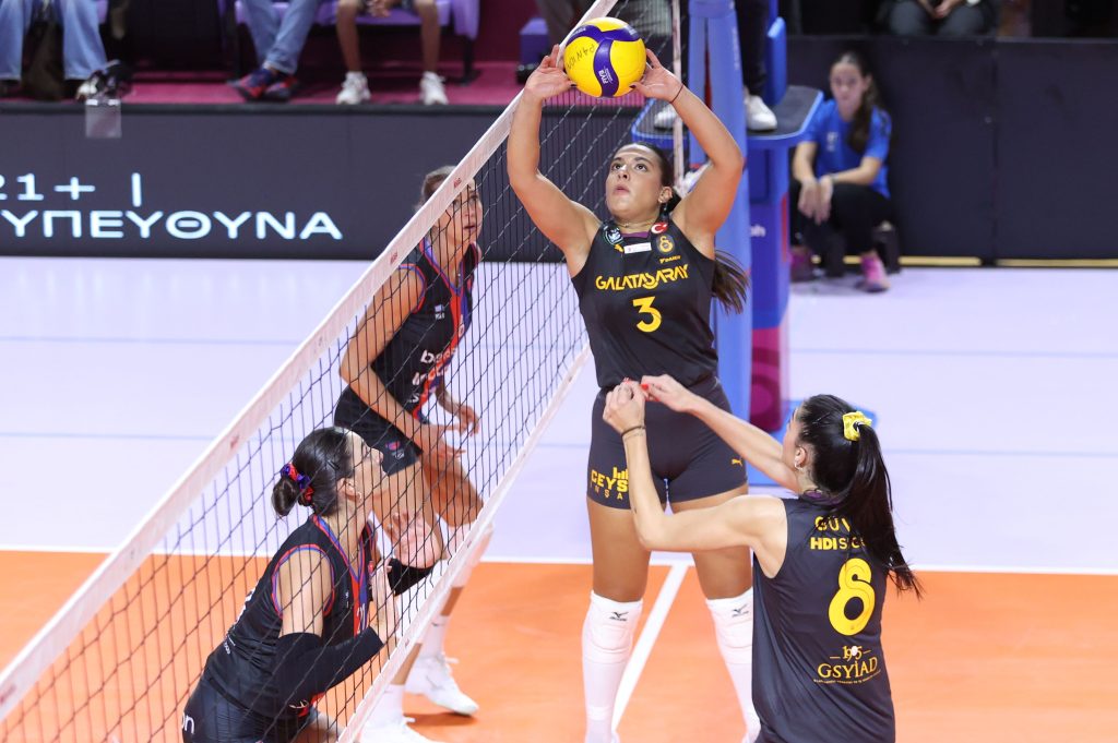 5359102 The Volley Lovers Women’s volleyball in action at the net: players in dark uniforms reach up to block/ hit the ball mid-air during a rally.