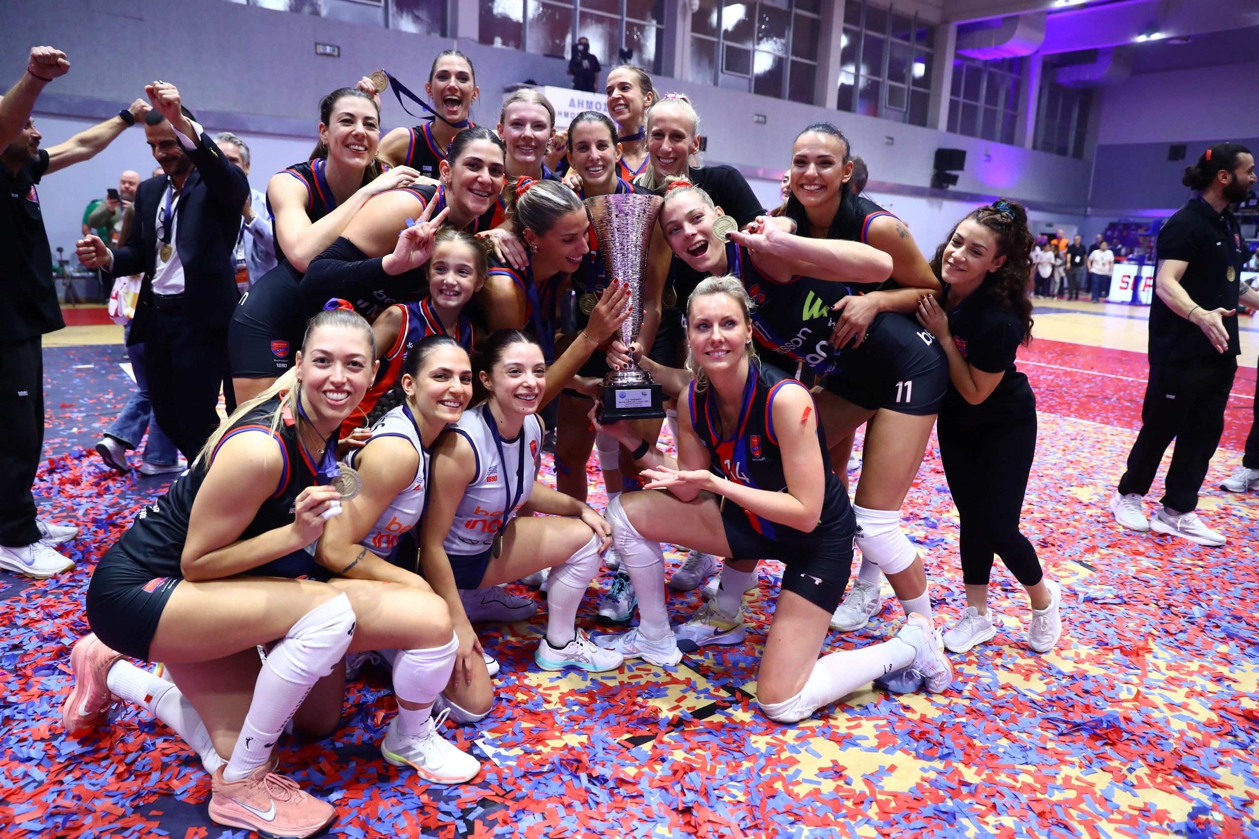 537815700 The Volley Lovers Female basketball team celebrates victory, posing with a large trophy and medals on a confetti-covered court.
