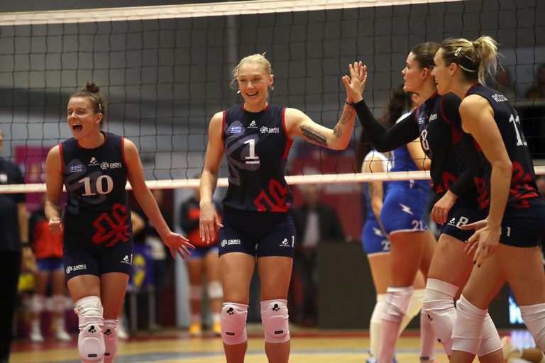538998000 The Volley Lovers Female volleyball players in navy uniforms celebrate with a high-five near the net during a match, smiling.
