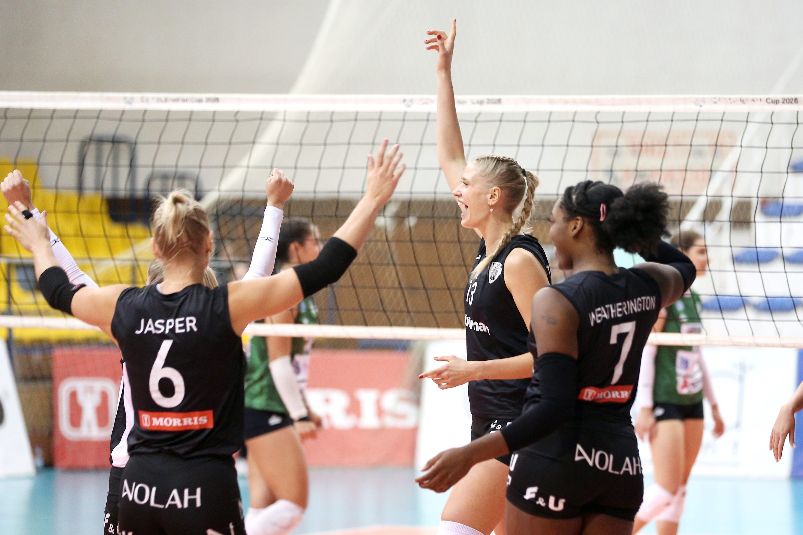 Volleyball players in black uniforms celebrate with a high-five at the net during a match.