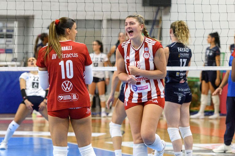 539023200 The Volley Lovers Two female volleyball players celebrate a point near the net during an indoor match; one in a red jersey #10 and the other in red-and-white stripes #13.