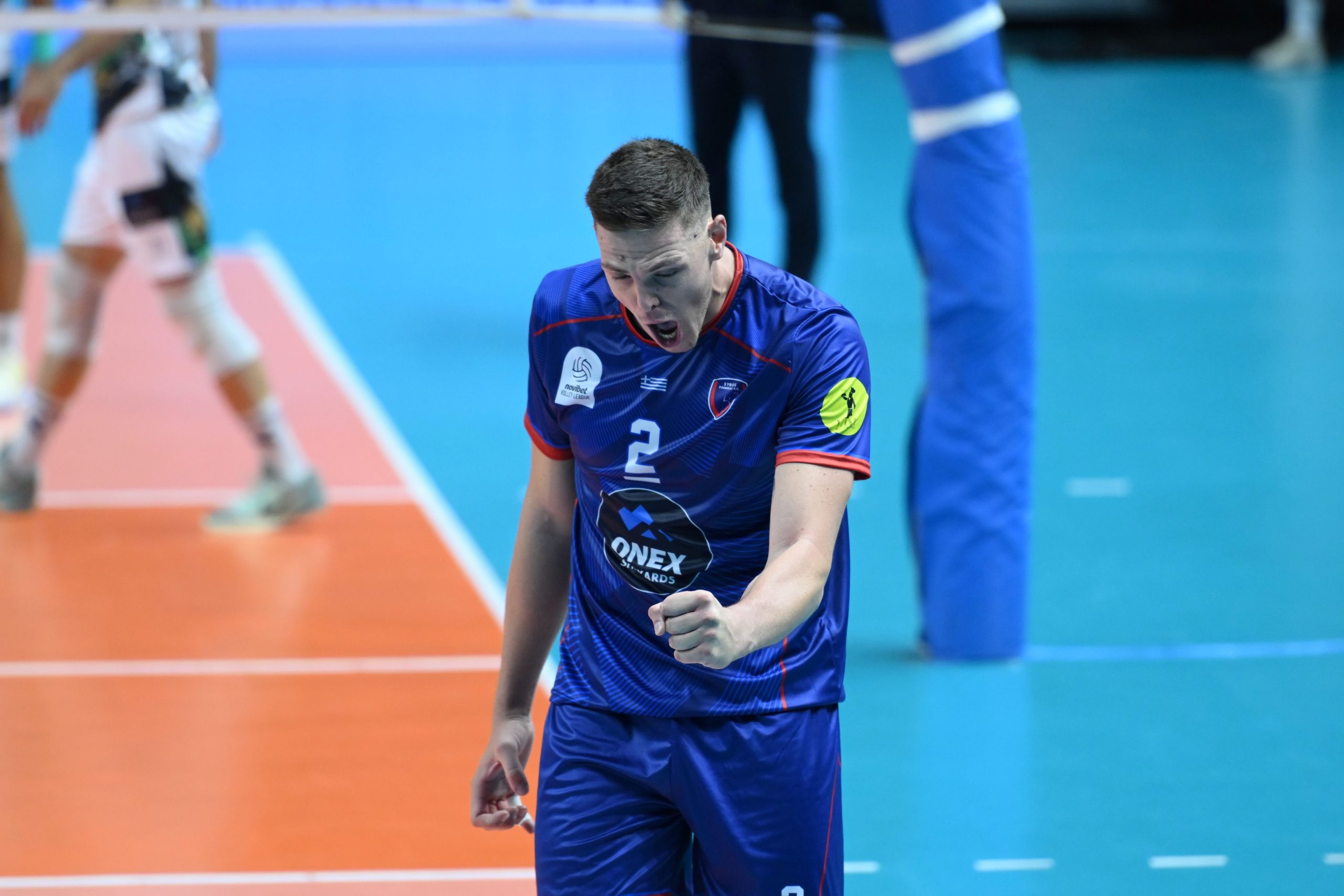 Volleyball player in a blue uniform celebrating with a clenched fist on an indoor court.