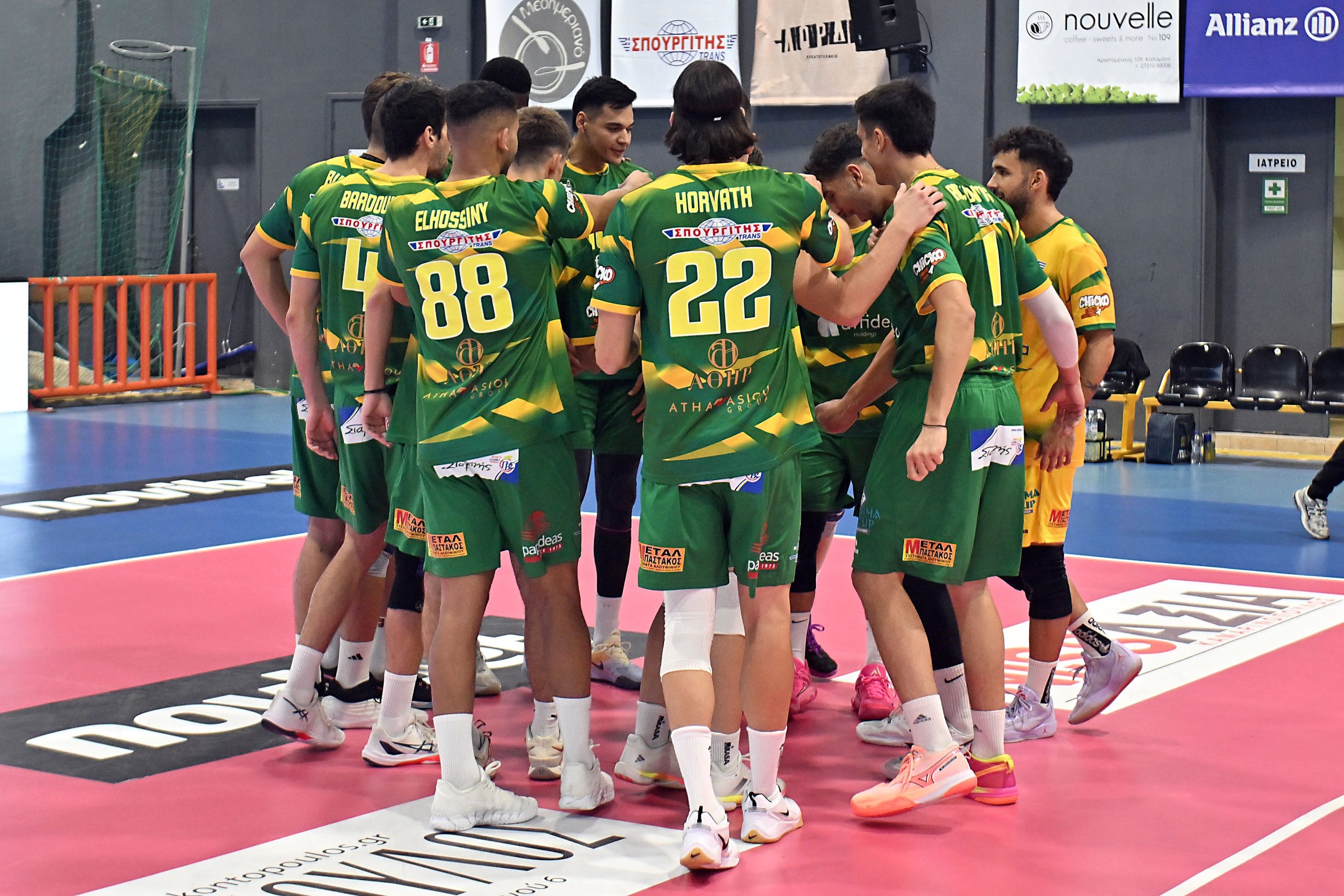 Group of male volleyball players in green and yellow uniforms huddling on a pink indoor court, with numbers 88 and 22 visible on their backs.