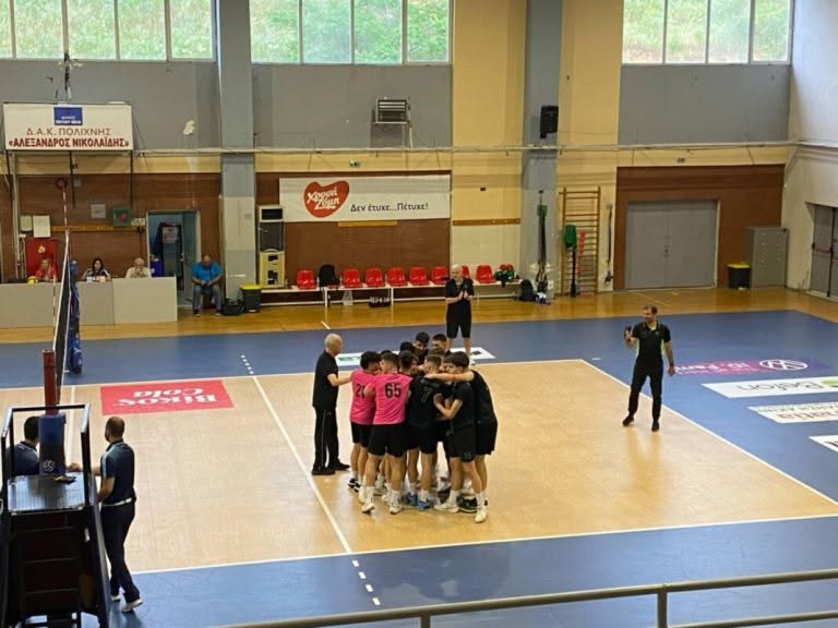 8432249764696314247356013816973576200118597n The Volley Lovers Volleyball team in pink and black jerseys huddles on an indoor court near the net, a coach guiding them. A referee and bench area are nearby.