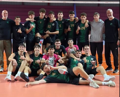 85442787147009177768956603634606303321363179n The Volley Lovers Youth volleyball team posing for a group photo in a gym, wearing green uniforms with coaches at either end, all smiling and giving thumbs up.