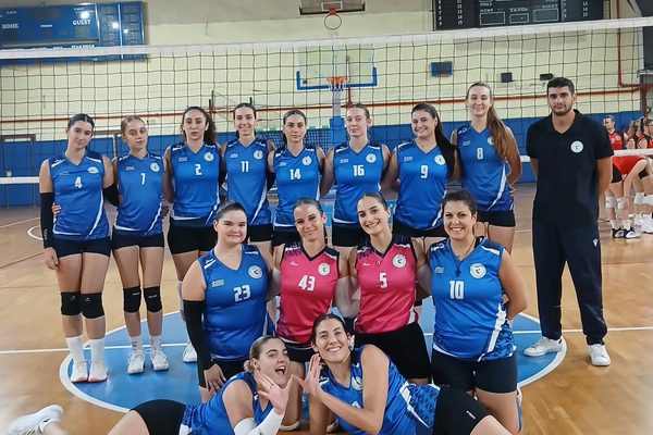 Group of female volleyball players in blue jerseys posing for a team photo in a gym, numbers visible on uniforms.