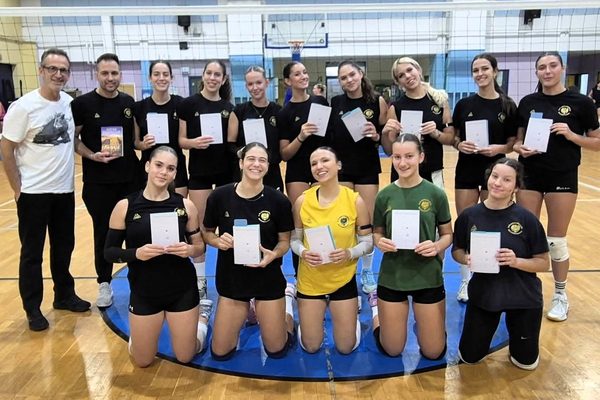 Volleyball team posing in a gym, each player holding a certificate and smiling at the camera, coach on the left.