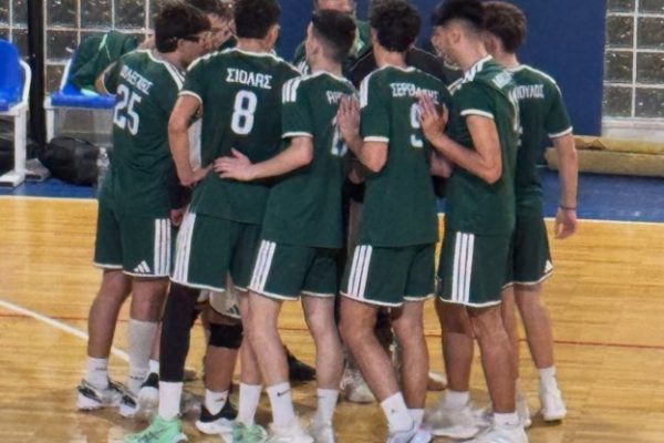 A group of male athletes in green uniforms huddles closely on an indoor court, arms around each other.