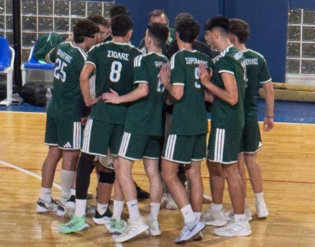 A group of male athletes in green uniforms huddles closely on an indoor court, arms around each other.