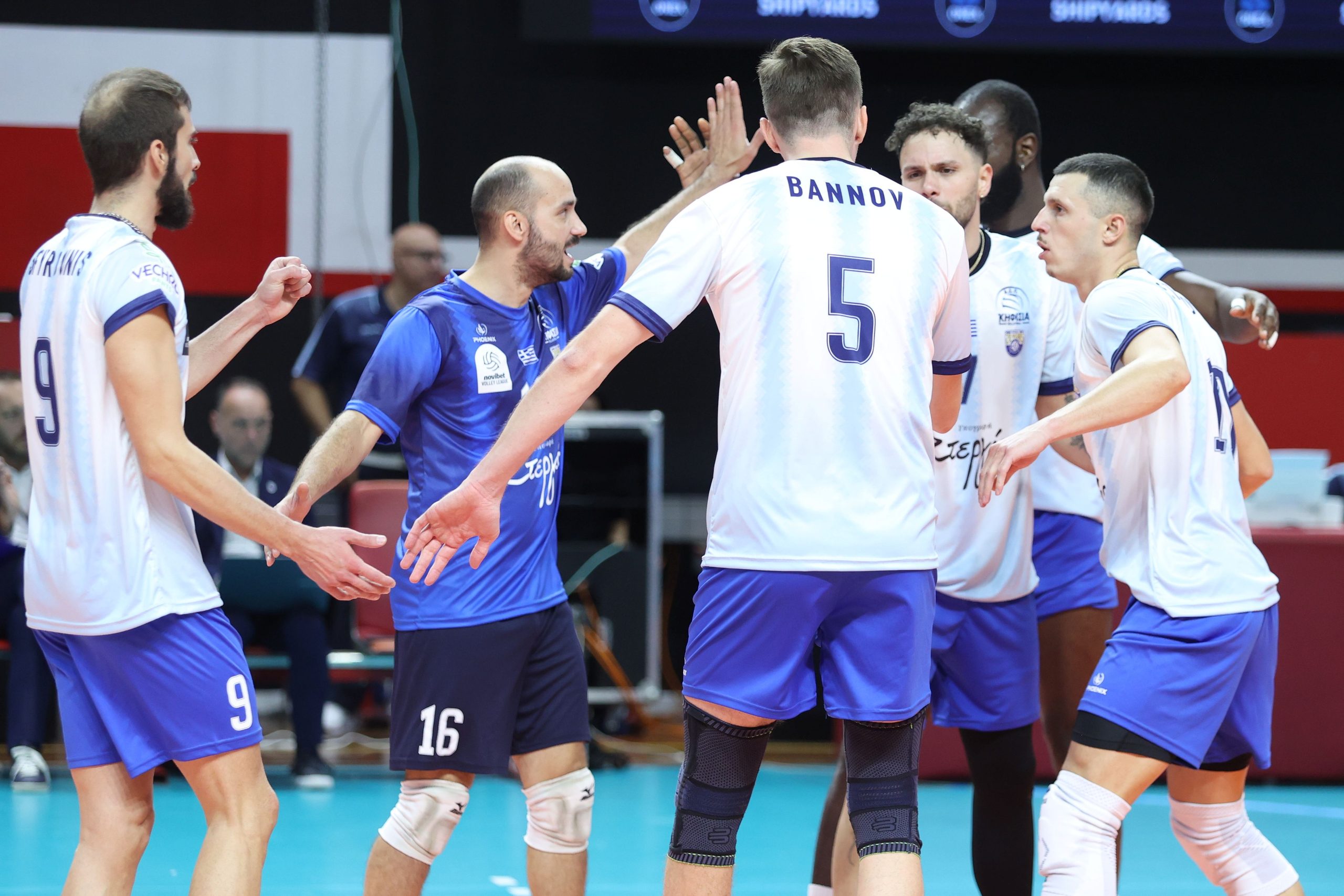 Volleyball players in white and blue uniforms high-fiving in a huddle on a court.