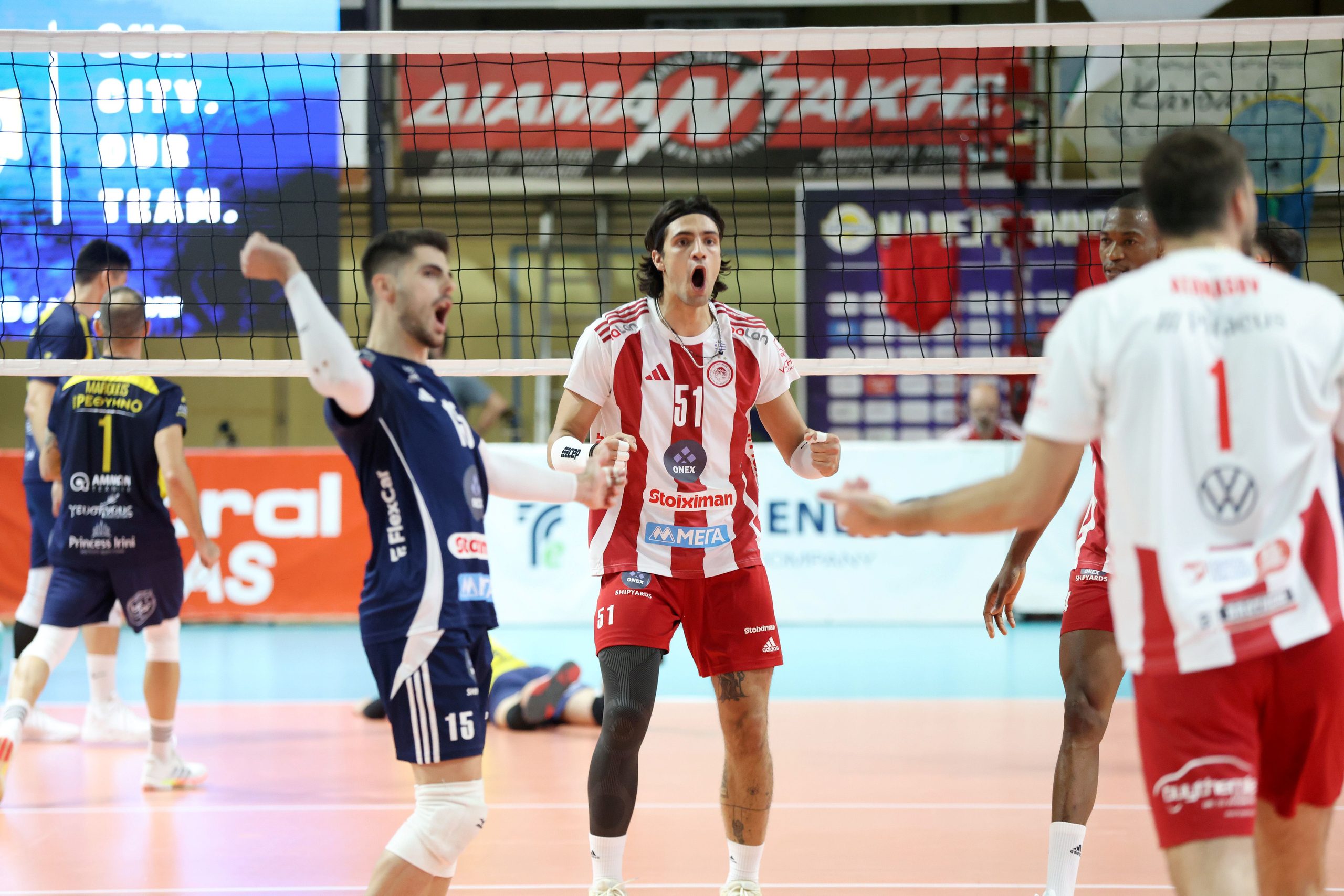 Volleyball players celebrate a point near the net; central player in red-and-white stripes with mouth open in celebration.