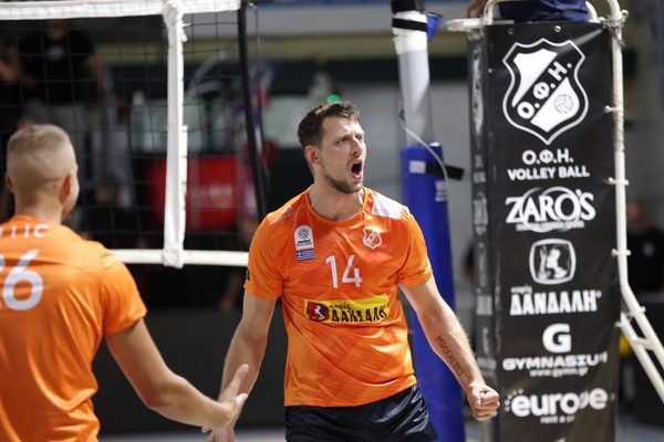 Male volleyball player in orange jersey #14 shouting with mouth open, celebrating a point near the net.